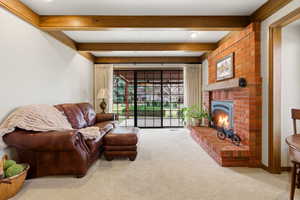 Living room with a brick fireplace, light carpet, and beam ceiling