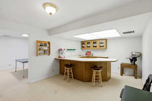 Indoor wet bar featuring light countertops, wood finish cabinets, light colored carpet, and glass fronted cabinets