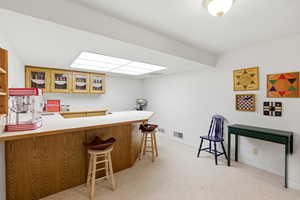 Bar area with light countertops, light carpet, wood finish cabinets, and glass fronted cabinets