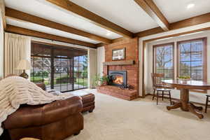 Living room with carpet flooring, a brick fireplace, healthy amount of natural light, and beam ceiling