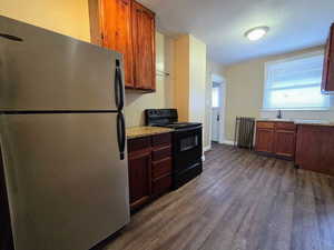 Kitchen featuring freestanding refrigerator, black range with electric stovetop, dark wood-style flooring, radiator, and light stone countertops