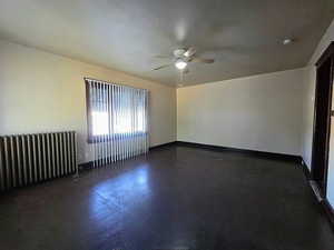Spare room featuring a ceiling fan, radiator, and dark wood-style flooring