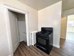 Kitchen with black gas range, dark wood finished floors, and radiator