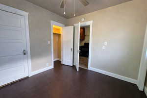Unfurnished bedroom with a walk in closet, dark wood-style floors, and ceiling fan