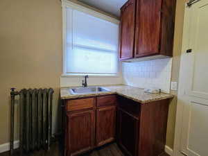 Kitchen with radiator heating unit, decorative backsplash, light stone counters, and dark wood-style flooring
