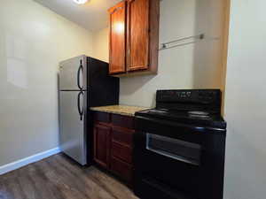 Kitchen featuring black range with electric cooktop, freestanding refrigerator, dark wood finished floors, light stone counters, and wood finish cabinetry