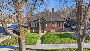 Bungalow-style home with brick siding, a shingled roof, a chimney, and a front lawn