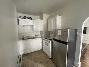 Kitchen featuring white cabinets, freestanding refrigerator, a baseboard radiator, electric range, and arched walkways
