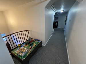 Recreation room with arched walkways, carpet, and a textured ceiling