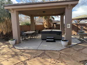 Fenced backyard featuring a patio, outdoor dining space, a hot tub, and a gazebo