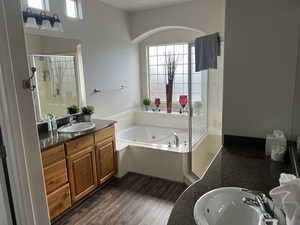Full bath with two vanities, a shower stall, a jetted tub, and dark wood-style floors