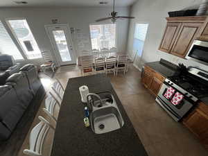 Kitchen featuring stainless steel appliances, open floor plan, dark tile patterned floors, wood finish cabinets, and a ceiling fan