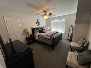 Bedroom with dark colored carpet, a ceiling fan, and a textured ceiling