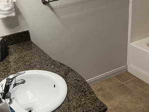 Full bathroom featuring a textured wall, vanity, dark tile patterned floors, and a tub