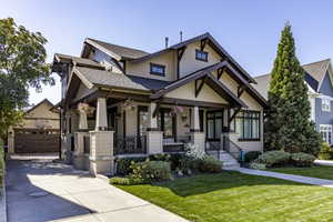 Craftsman-style home featuring roof with shingles, a porch, a front lawn, and an outbuilding