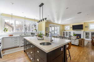 Kitchen featuring a kitchen breakfast bar, a warm lit fireplace, open floor plan, a kitchen island with sink, and light stone countertops