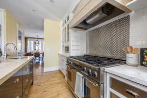Kitchen with range hood, dual tone cabinetry, stainless steel appliances, light wood finished floors, and glass insert cabinets