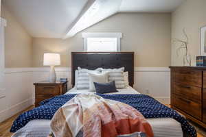 Bedroom featuring vaulted ceiling, wainscoting, and wood finished floors