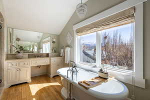 Full bath featuring vanity, suspended lighting, light wood finished floors, vaulted ceiling, and a soaking tub