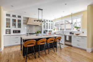 Dual tone kitchen featuring glass fronted cabinets, two tone cabinetry, a breakfast bar area, a kitchen island with sink, and light wood-style floors
