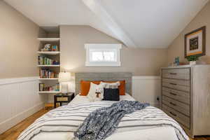 Bedroom featuring wainscoting, light wood-type flooring, and lofted ceiling