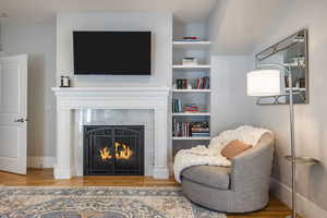 Living area featuring a warm lit fireplace, light wood-style flooring, and built in shelves