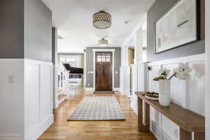 Entryway with light wood-style flooring, ornate columns, a wainscoted wall, and a decorative wall