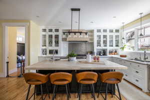 Dual tone kitchen with glass insert cabinets, two tone color scheme, a kitchen breakfast bar, a center island with sink, and open shelves