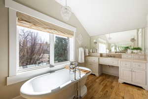Bathroom with vanity, suspended lighting, light wood-style floors, a freestanding tub, and lofted ceiling