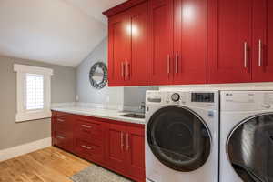 Laundry area featuring lofted ceiling, washer and dryer, light wood finished floors, and cabinet space