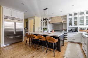 Two tone kitchen with glass insert cabinets, stainless steel appliances, a kitchen bar, two tone cabinetry, and pendant lighting