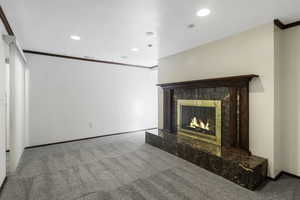 Unfurnished living room featuring crown molding, light carpet, a premium fireplace, and recessed lighting