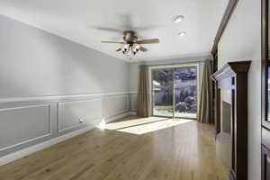 Unfurnished room featuring a decorative wall, a wainscoted wall, ceiling fan, light wood finished floors, and ornamental molding