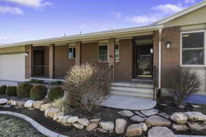 Property entrance with covered porch, brick siding, and a garage