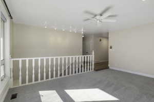 Carpeted spare room featuring a ceiling fan and rail lighting
