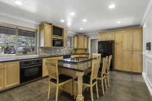 Kitchen featuring light wood finish cabinets, crown molding, black appliances, a center island, and a breakfast bar area