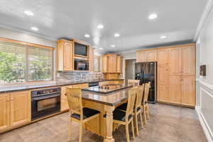 Kitchen featuring light wood finish cabinets, black appliances, a kitchen breakfast bar, a kitchen island, and dark stone countertops