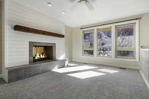 Unfurnished living room featuring a tiled fireplace, carpet floors, and a ceiling fan