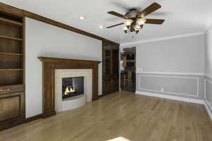 Unfurnished living room with light wood finished floors, crown molding, ceiling fan, a premium fireplace, and built in features