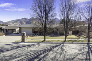 Ranch-style home featuring a front yard, a mountain view, concrete driveway, and a garage