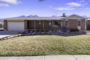 Ranch-style house with covered porch, brick siding, a front lawn, an attached garage, and driveway