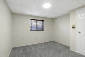 Carpeted empty room featuring a drop ceiling and baseboards