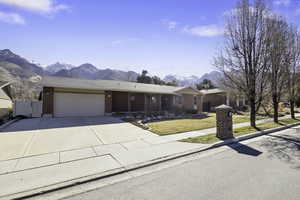 Single story home with a mountain view, an attached garage, driveway, a front lawn, and brick siding