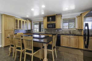 Kitchen featuring crown molding, a breakfast bar, black appliances, a center island, and dark stone countertops