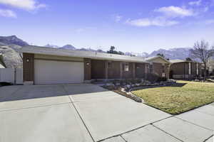 Ranch-style house featuring a mountain view, brick siding, concrete driveway, a garage, and a front yard