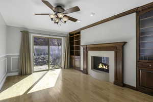 Unfurnished living room with light wood-style floors, built in shelves, ceiling fan, crown molding, and a multi sided fireplace