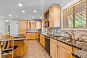 Kitchen with light wood finish cabinetry, ornamental molding, glass fronted cabinets, tasteful backsplash, and dark stone counters