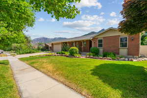 Single story home featuring a porch, a garage, brick siding, a front yard, and a mountain view