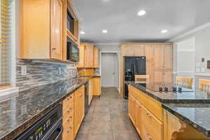 Kitchen featuring light wood finish cabinets, dark stone countertops, ornamental molding, recessed lighting, and black appliances