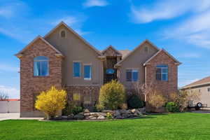 View of front of home with a front lawn, stucco siding, stone siding, and brick siding